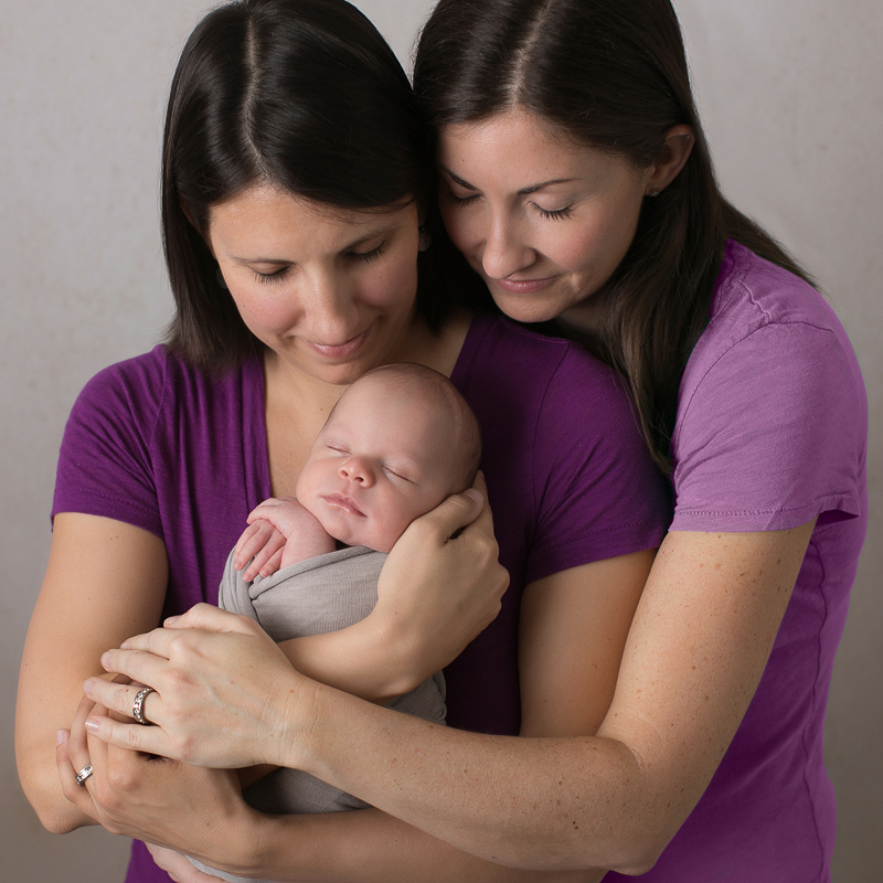 Lesbian family holding their newborn baby wearing purple shirts